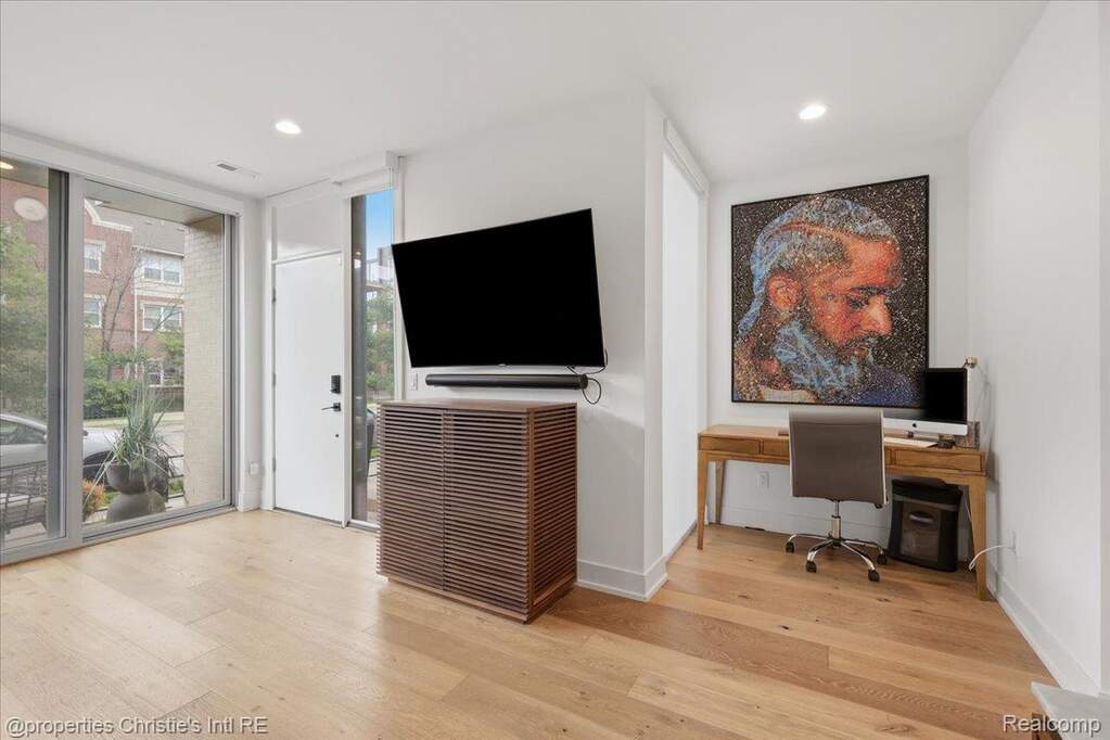 Hardwood-finish flooring throughout, featuring a full-light entry door, recessed ceiling lighting, and a dedicated corner desk area