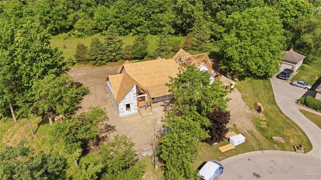 New construction residential property featuring partial roofing installation, rough framing, and a natural tree-lined perimeter