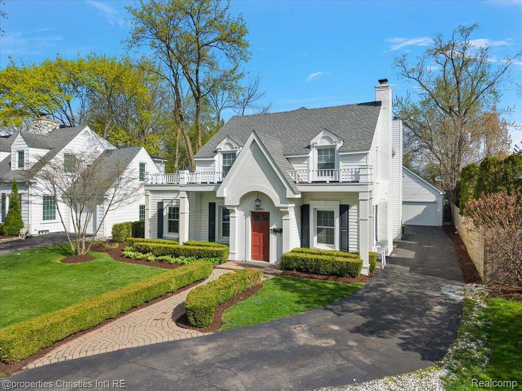 View of front facade featuring a chimney, a balcony, a shingled roof, and a front lawn