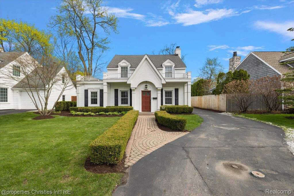 New england style home featuring a balcony, asphalt driveway, and a chimney