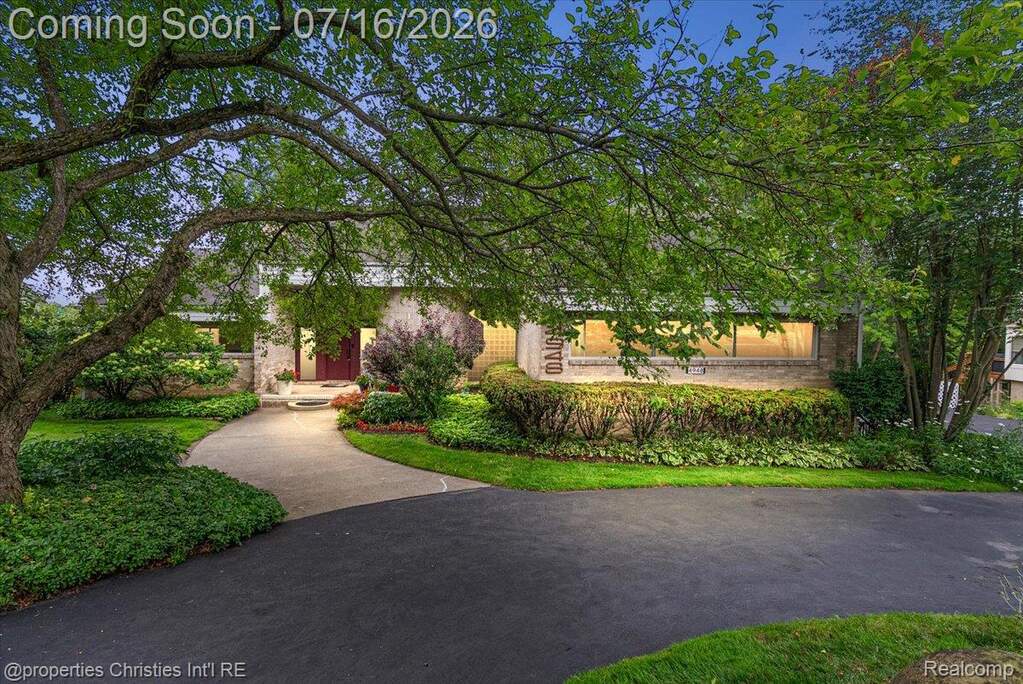 Manicured front yard with mature trees and a paved driveway