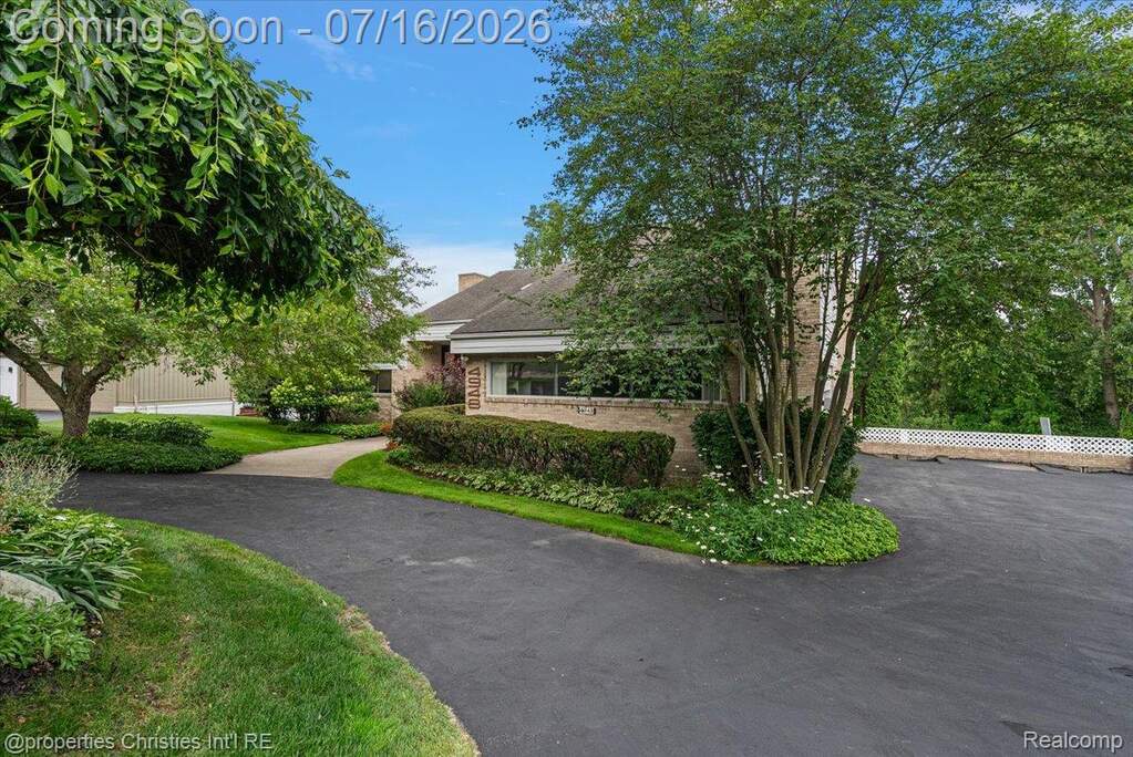 Asphalt driveway with manicured landscaping, mature trees, and a brick exterior building