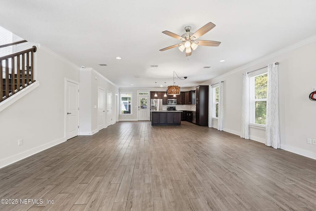 Living Area and Kitchen View – Open-concept main level highlighted by wood-look tile flooring, recessed lighting, and generous natural light flowing toward the kitchen