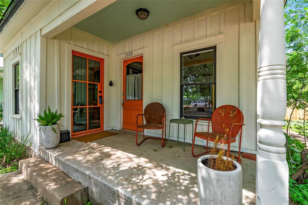 The front porch sets the tone fast, with bold orange doors, vintage seating, leafy shade, and the kind of curb appeal that feels more personal than polished.