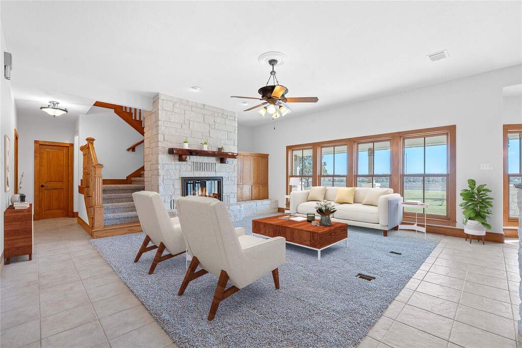 Living room with a stone fireplace, stairs, a ceiling fan, and light tile patterned floors
