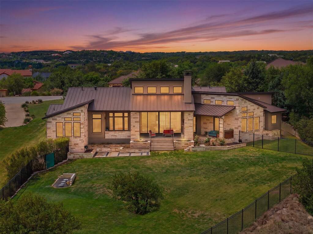 At dusk, the home settles into the landscape with a quiet confidence, glowing from within and opening outward to uninterrupted hill country views that feel expansive and private all at once.