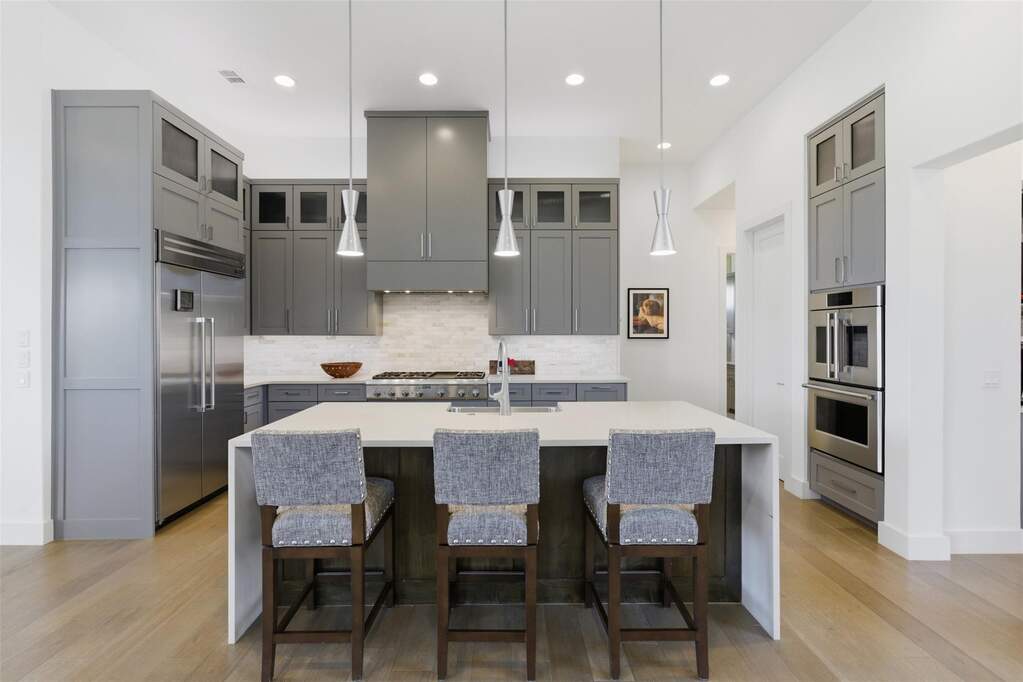 The kitchen reads as both architectural and inviting, with full-height cabinetry, balanced symmetry, and a waterfall island.