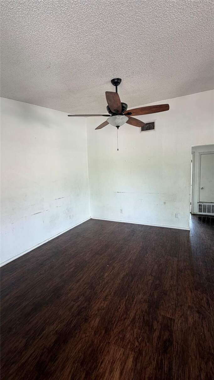 Empty room with a textured ceiling, dark wood-type flooring, and ceiling fan