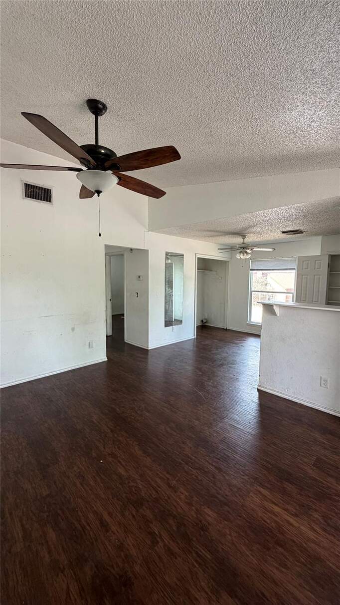 Unfurnished living room with a textured ceiling, a ceiling fan, and dark wood finished floors