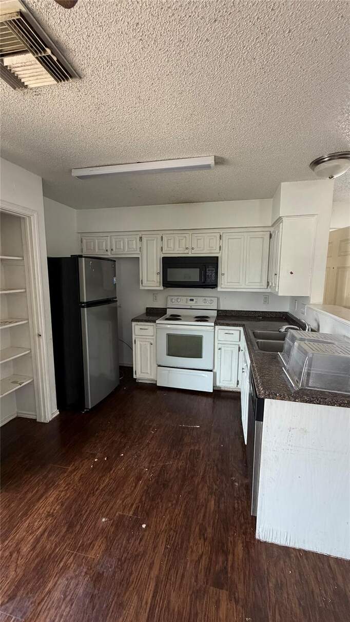 Kitchen featuring freestanding refrigerator, white electric range oven, white cabinetry, black microwave, and dark wood-style flooring