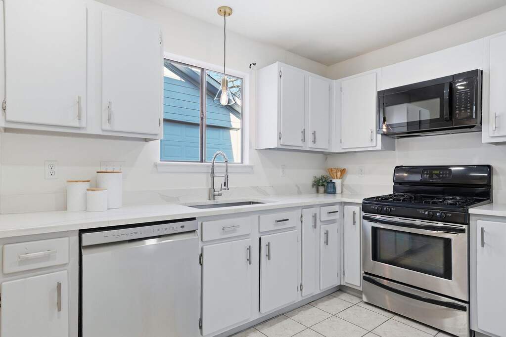 Kitchen featuring stainless steel range with gas stovetop, black microwave, dishwasher, and white cabinetry