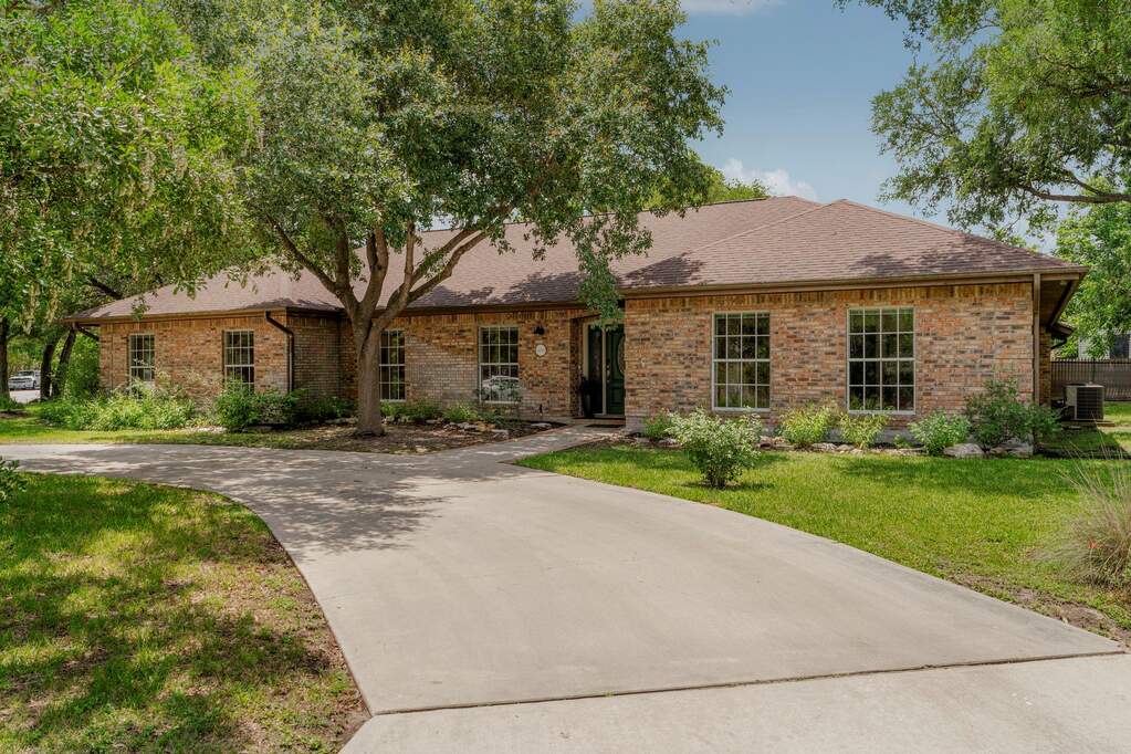 Mature trees frame this brick residence with an inviting front entry and paved driveway.