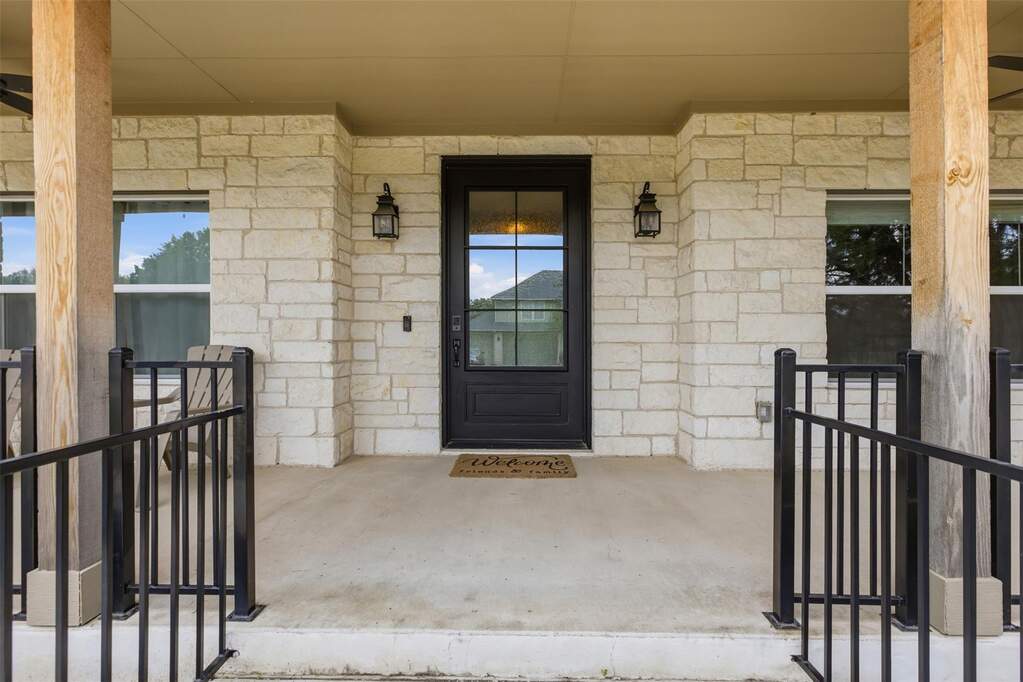 Front porch entry featuring stone exterior, dark wood-finish door with glass inserts, two exterior light fixtures, and black metal railings