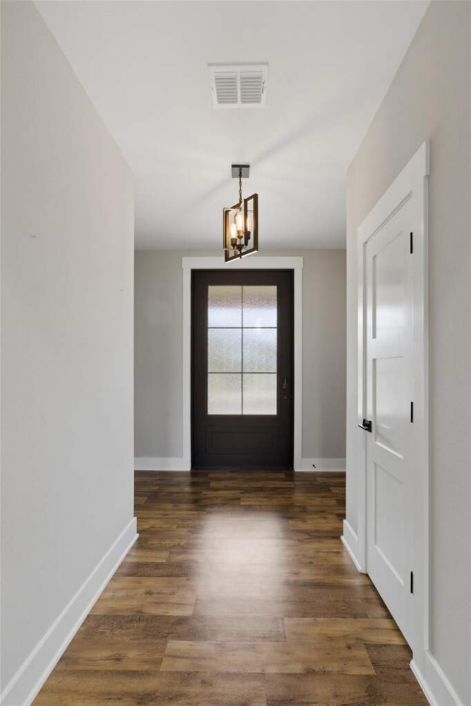 Entryway featuring wood-finish flooring, a contemporary pendant light fixture, and a dark-paneled door with frosted glass