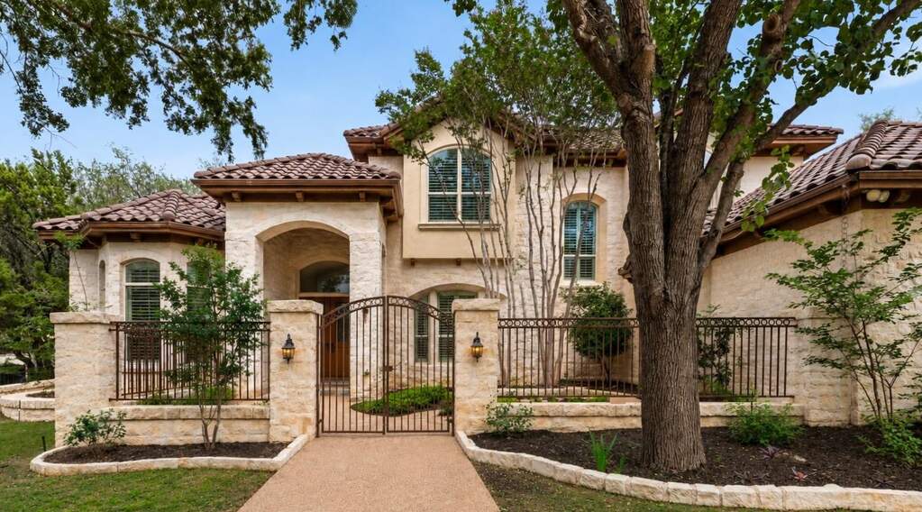 A grand entrance awaits behind a wrought iron gate, revealing an elegant stone and stucco facade with a terracotta tile roof.