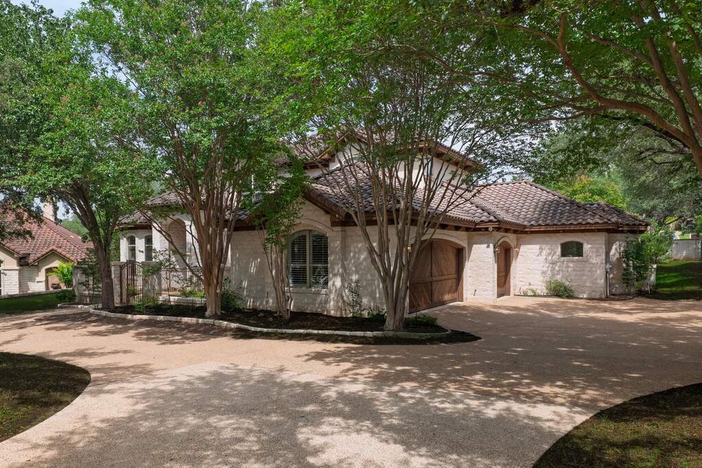 Inviting front elevation with arched windows, tile roof, and a natural canopy of mature trees.garage door