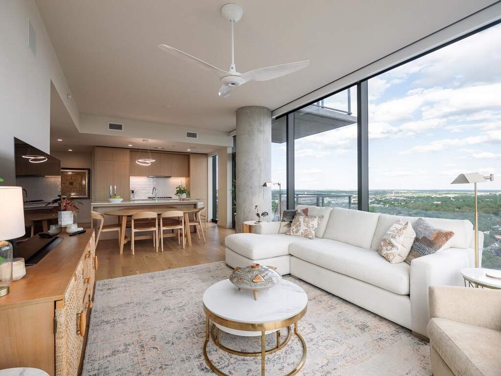 This open-concept living space features expansive windows with panoramic views, light hardwood flooring, and a modern ceiling fan