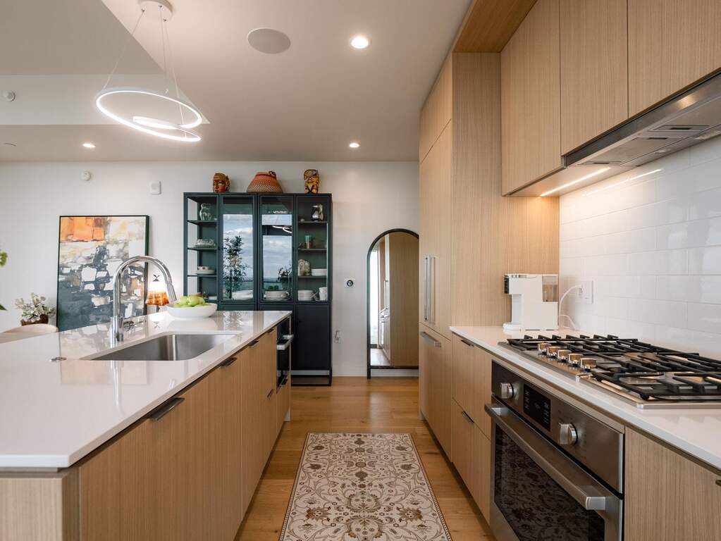 Modern kitchen featuring light wood cabinetry, stainless steel appliances, a white subway tile backsplash, and a large island with a sink and white countertop