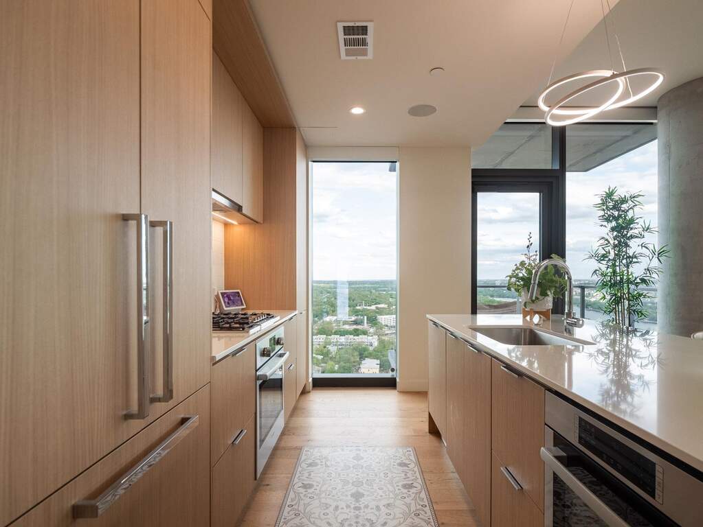 Modern kitchen featuring light wood cabinetry, integrated appliances, a central island with a sink, and expansive windows offering outdoor views