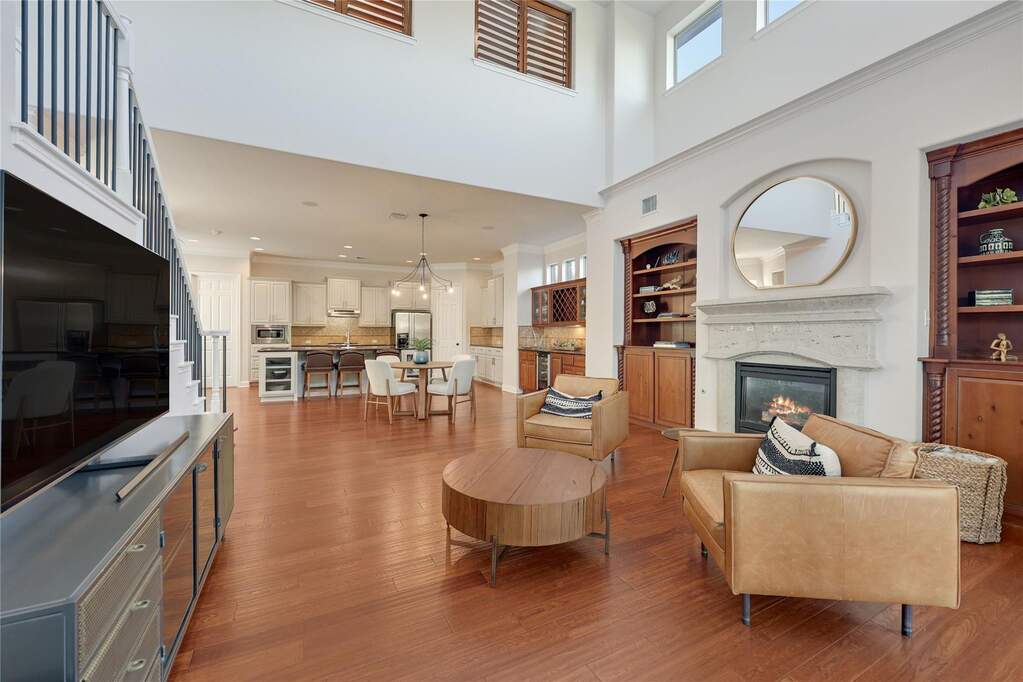 The open-concept living room includes soaring ceilings, built-in cabinetry, a cozy fireplace, and seamless flow into the kitchen and dining spaces