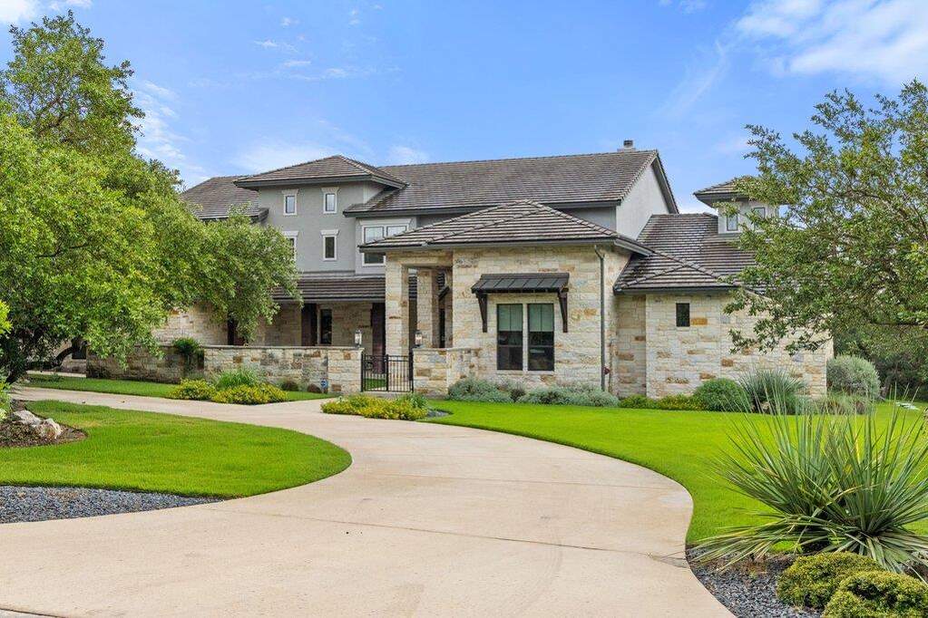 Too grand to capture in a single shot- A graceful driveway leads to a stone and stucco home, framed by lush landscaping and mature trees.
