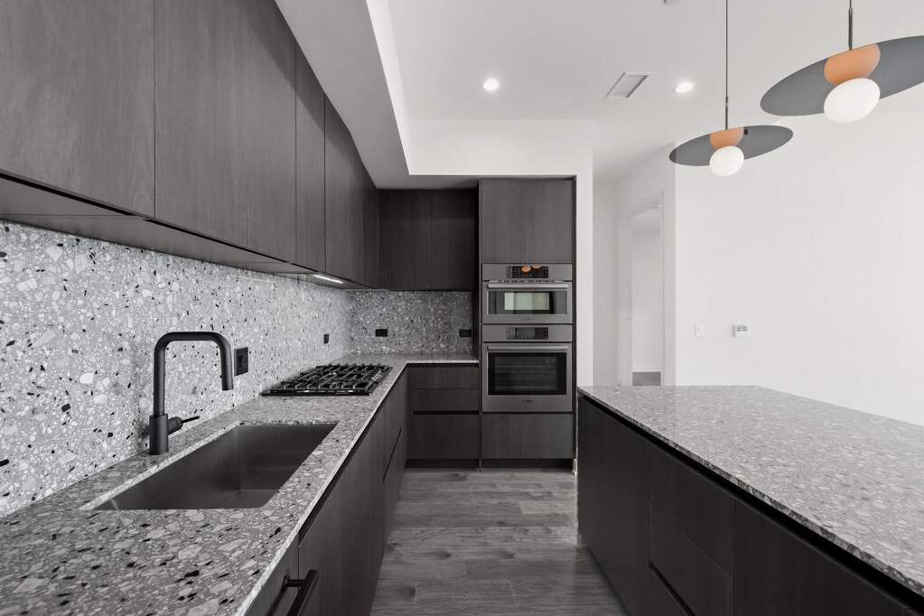 Kitchen featuring custom Italkraft cabninetry, terrazzo backsplash, waterfall-edge terrazzo countertops, built-in stainless steel Bosch appliances, and pendant lighting above kitchen island.