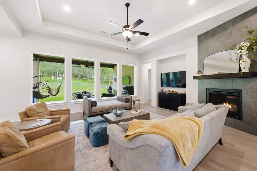 The living room opens up under a tray ceiling, drawing you in to relax on the couch while a wall of windows floods the entire space with warm, natural light