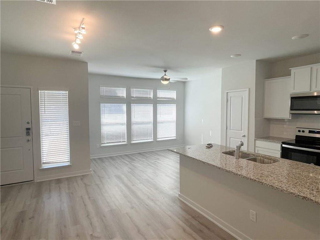 Open-concept living space featuring wood-finish flooring, a kitchen island with dual basin sink and granite-style countertop, white cabinetry, a full suite of stainless steel appliances, and 