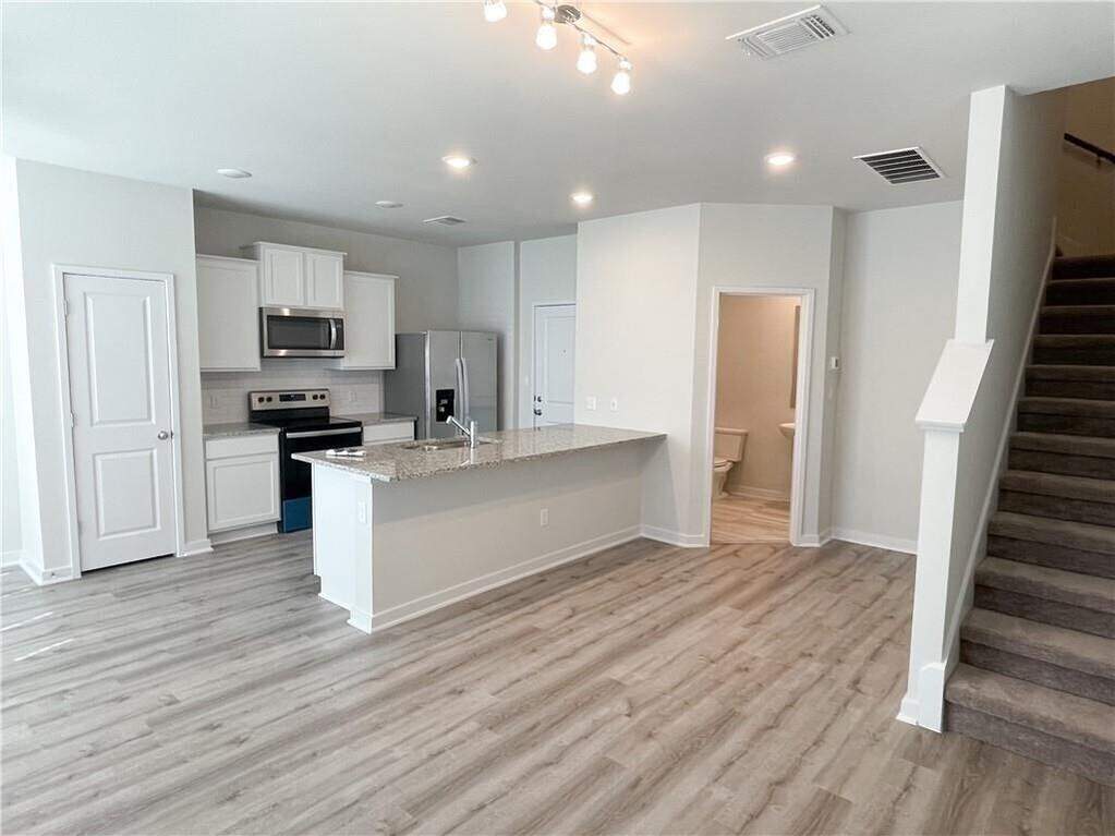 Open-concept living space with wood-finish flooring, a kitchen island featuring a light-toned countertop, white cabinetry, and stainless steel appliances