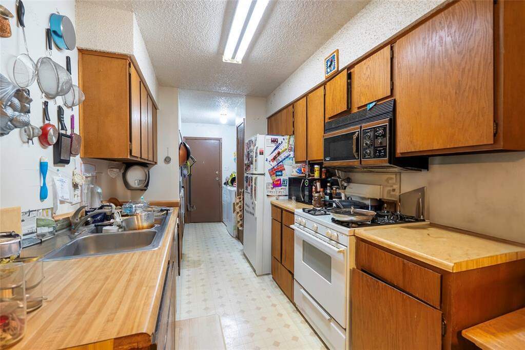 Kitchen featuring light flooring, wood finish cabinetry, white appliances, light countertops, and a textured ceiling