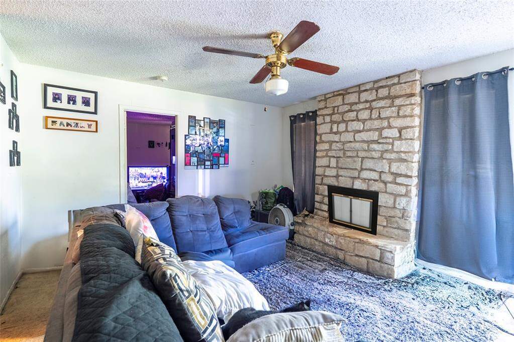 Carpeted living room with a textured ceiling, a stone fireplace, and ceiling fan