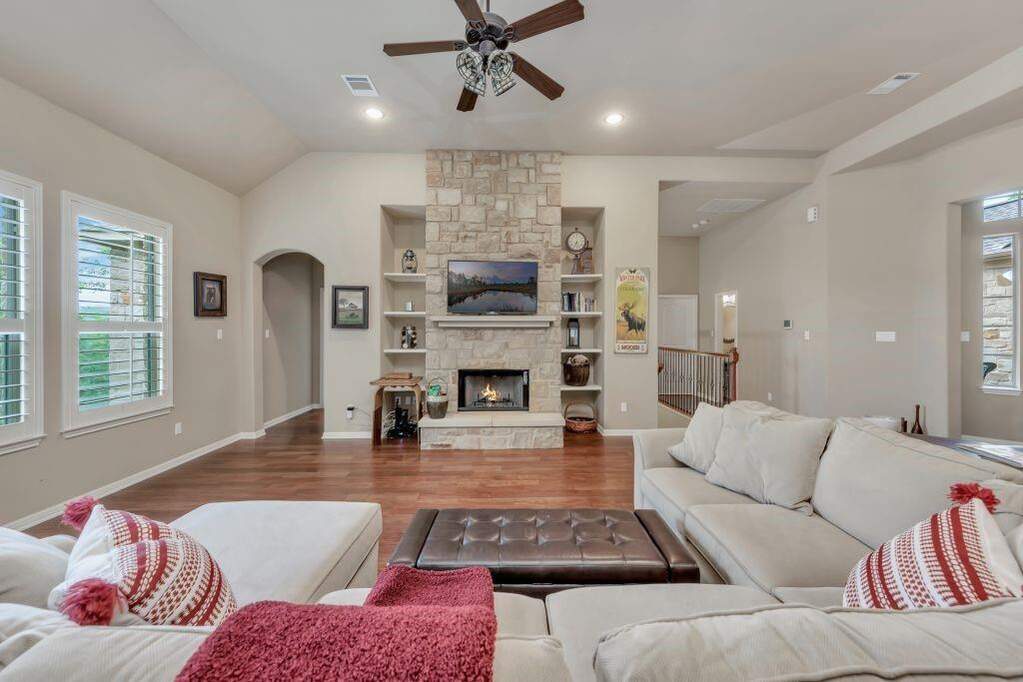 Living room with plenty of natural light, ceiling fan, wood finished floors, a fireplace, and lofted ceiling