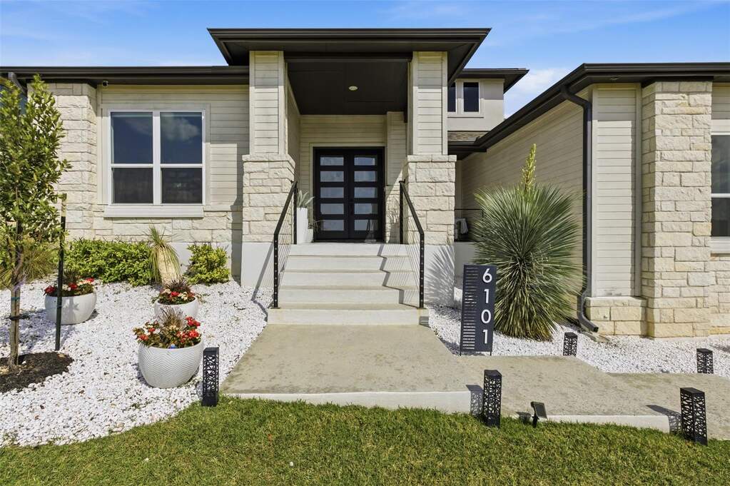 View of exterior entry with covered patio, glass-panel double doors, and landscaped front beds with pathway lighting.
