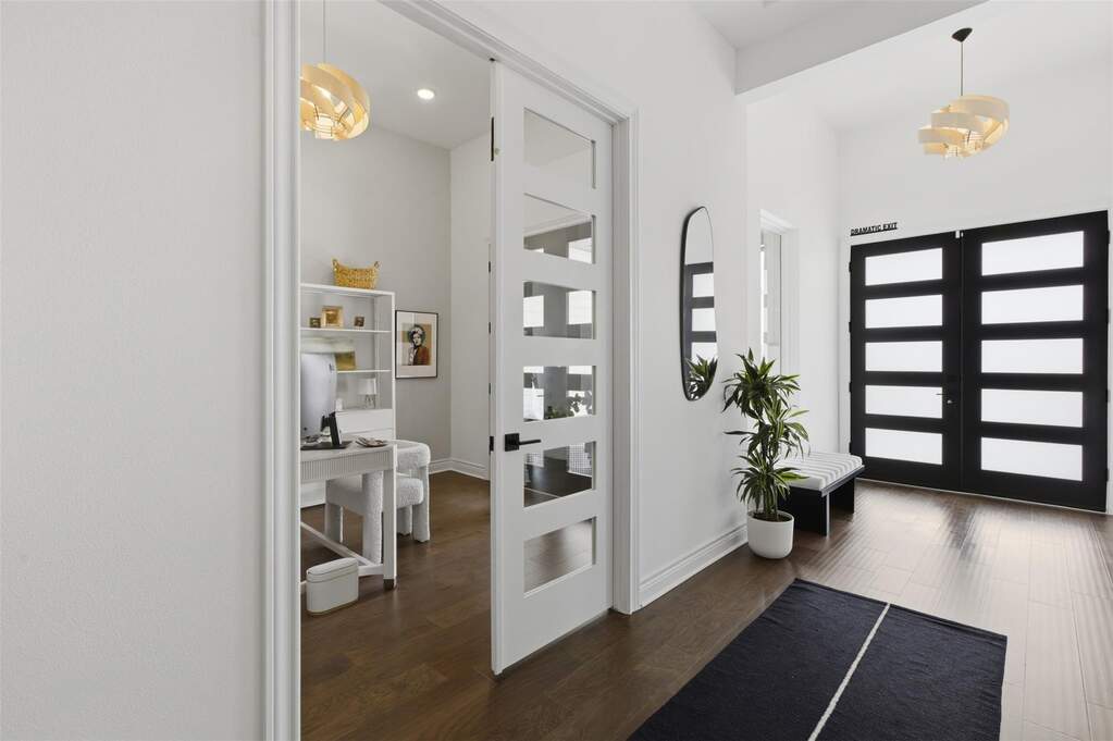 Entry foyer with glass-panel double doors, dark hardwood floors, and high ceilings. Glass-panel French doors open to a dedicated home office with built-in shelving and pendant lighting.