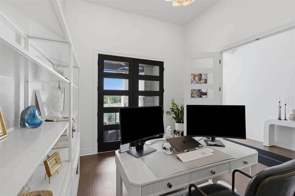 Private office with glass-panel French doors, dark hardwood floors, open shelving, and direct access to covered patio.
