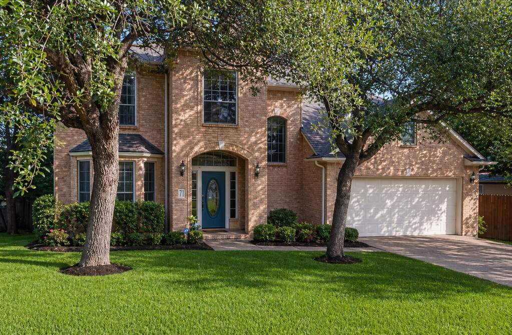 Traditional brick-clad exterior featuring a prominent arched entry with a contrasting blue door, a bay window with multiple panes, a two-car garage, and a lush green lawn.