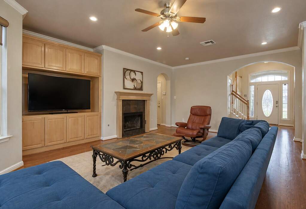 Living area featuring hardwood flooring, built-in cabinetry, a fireplace with a stone surround, recessed lighting, and a ceiling fan.