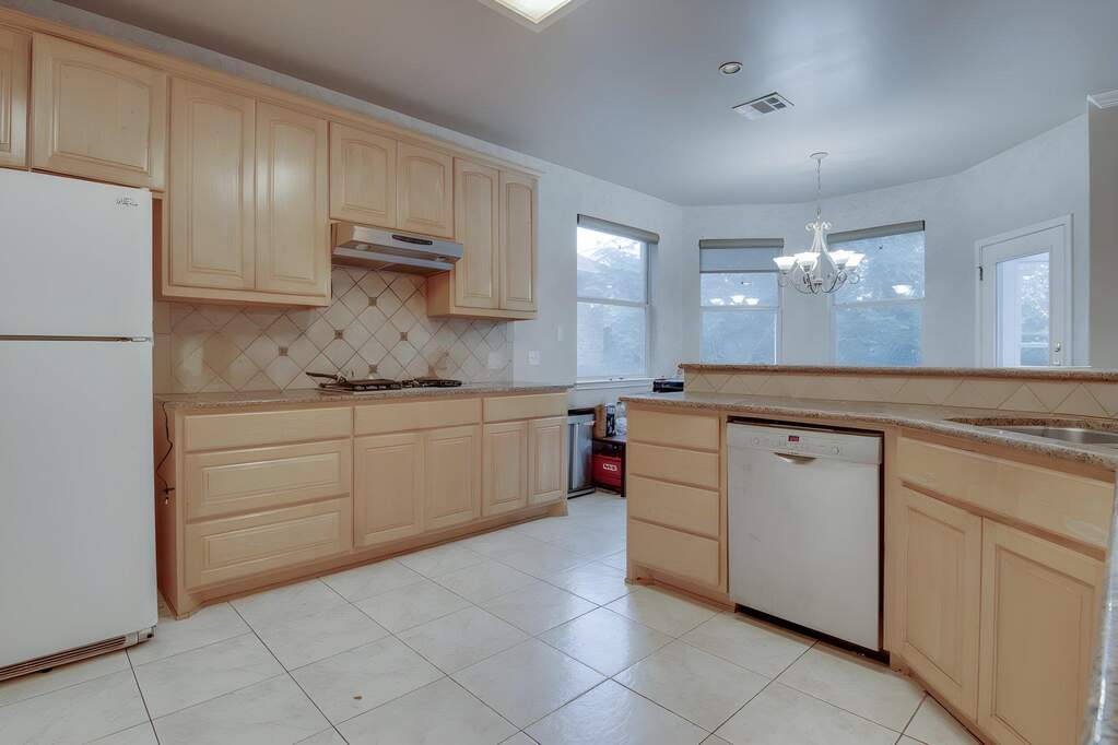 Kitchen featuring ample light wood-finish cabinetry, a tile backsplash with a diamond pattern, and a built-in stainless steel dishwasher.