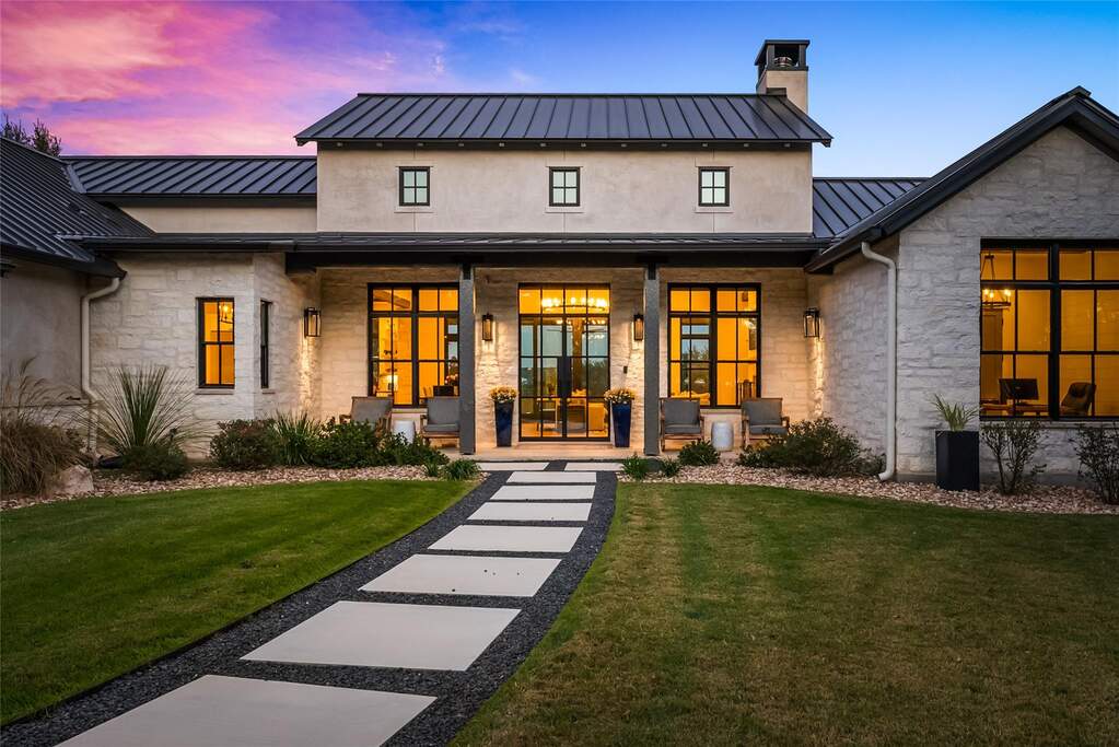 A modern stepping stone walkway creates a dramatic approach to the covered porch, where inviting seating and soft exterior lighting highlight the home’s upscale, welcoming character.