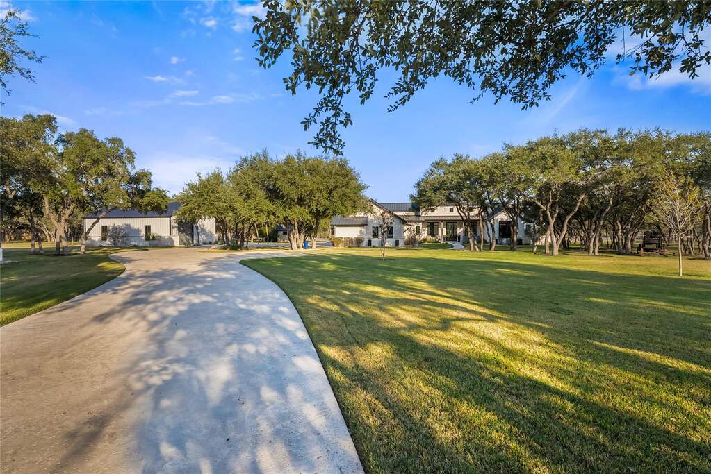 The expansive front acreage offers a serene, park like setting with wide open green space and a sweeping, curved driveway that guides you toward a stunning ranch style residence.