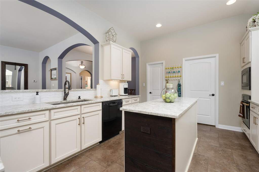 Kitchen with black appliances, a kitchen island, light stone counters, a sink, and backsplash