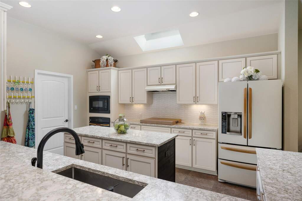 Kitchen featuring tasteful backsplash, black appliances,  under cabinet range hood, lofted ceiling with skylight, and a sink