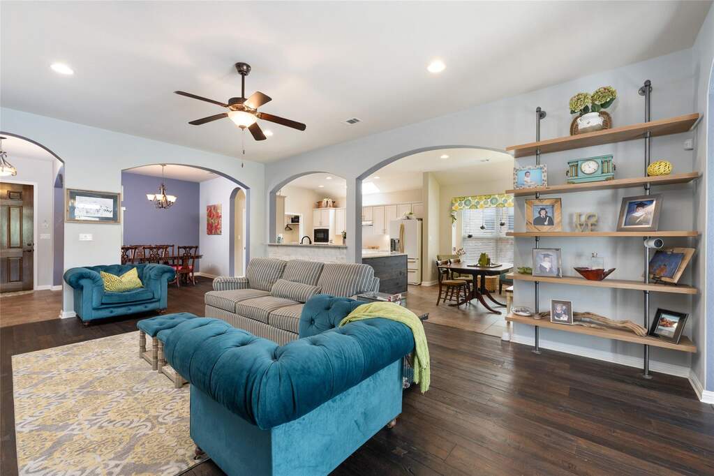 Living area with baseboards, visible vents, arched walkways, wood flooring, and ceiling fan