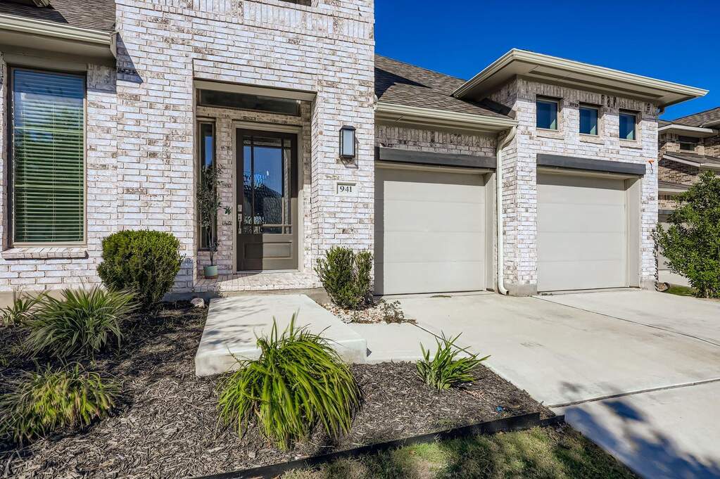 Doorway to property with concrete driveway, brick siding, a shingled roof, and stone siding
