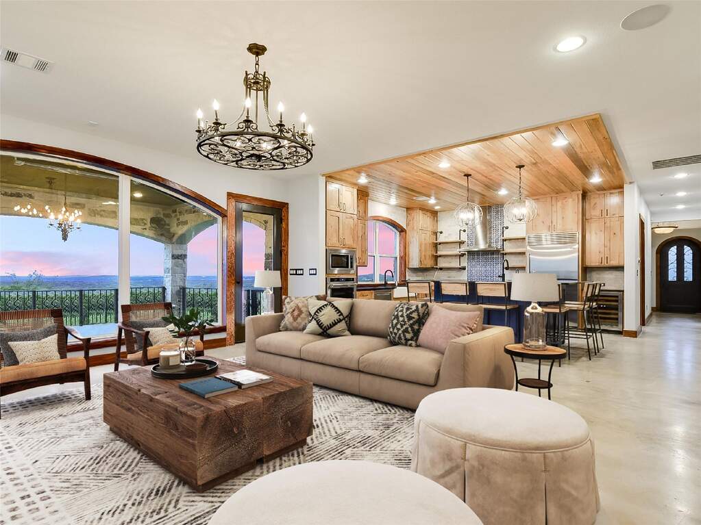 Open-concept living and kitchen area with gracefully arched windows, a statement chandelier, and direct access to the deck.