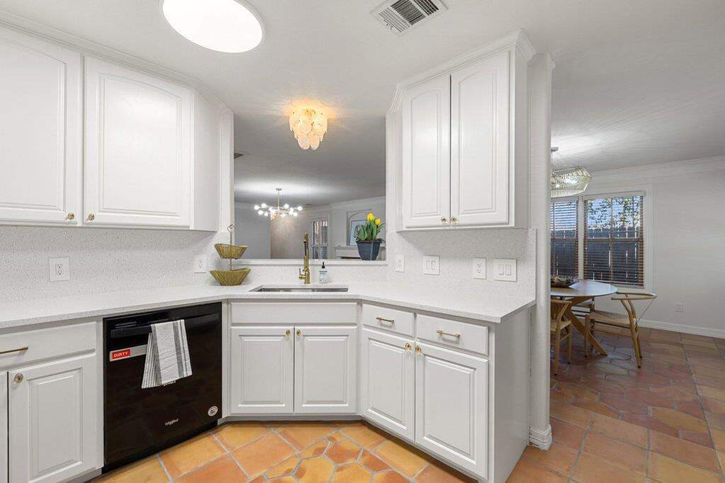 Kitchen featuring hanging lights, white cabinets, dishwasher, and ornamental molding