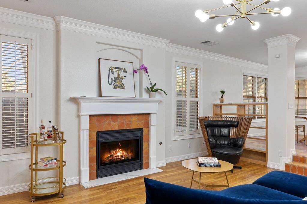 Living area with suspended lighting, ornamental molding, light wood finished floors, and a tile fireplace