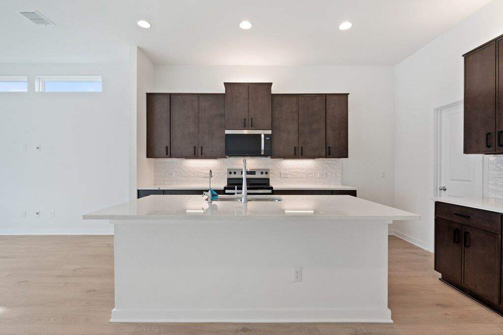 Kitchen featuring dark wood finish cabinets, tasteful backsplash, a center island with sink, stainless steel appliances, and recessed lighting
