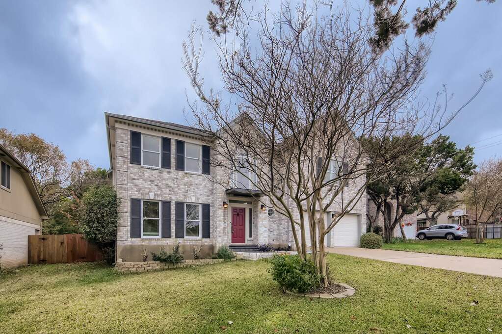 A classic brick-front home with a welcoming red entry door and a well-tended green lawn.