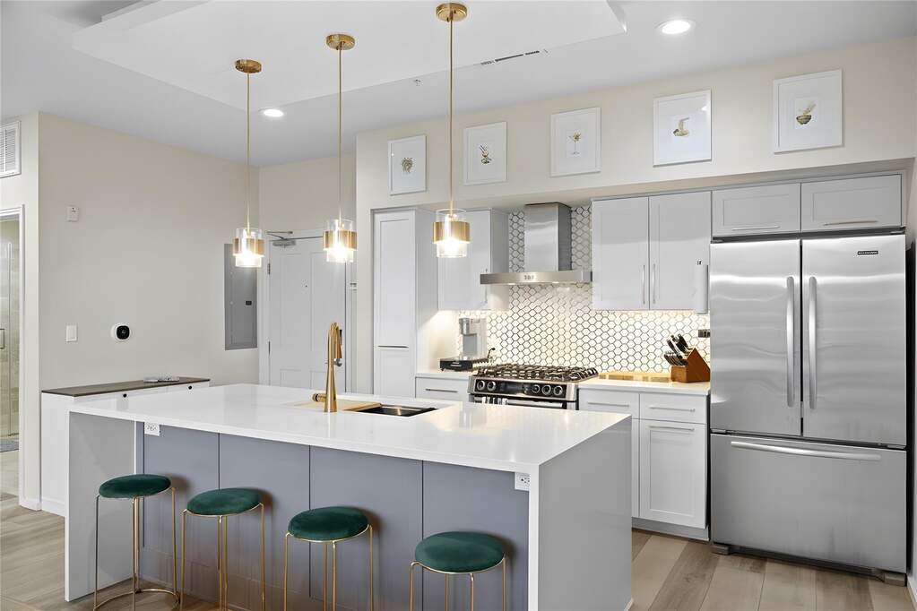 The kitchen blends modern updates with thoughtful design, anchored by a waterfall island and surrounded by brass accents, designer cabinetry, and warm natural light